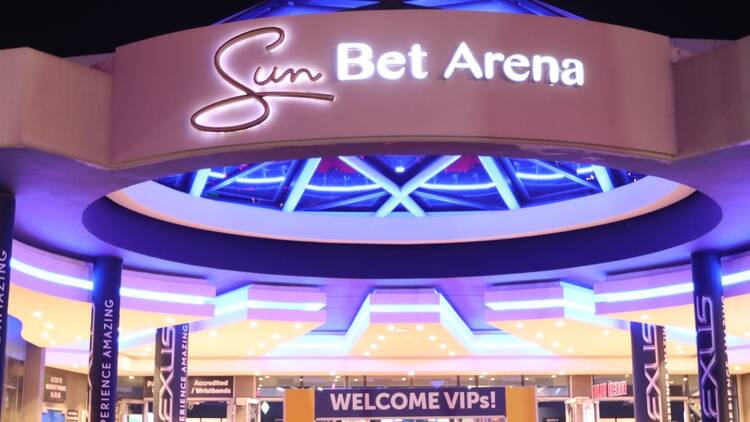 Exterior view of the Sun Bet Arena entrance with purple neon lights and a circular overhang, giving a vibrant, glowing look at night.