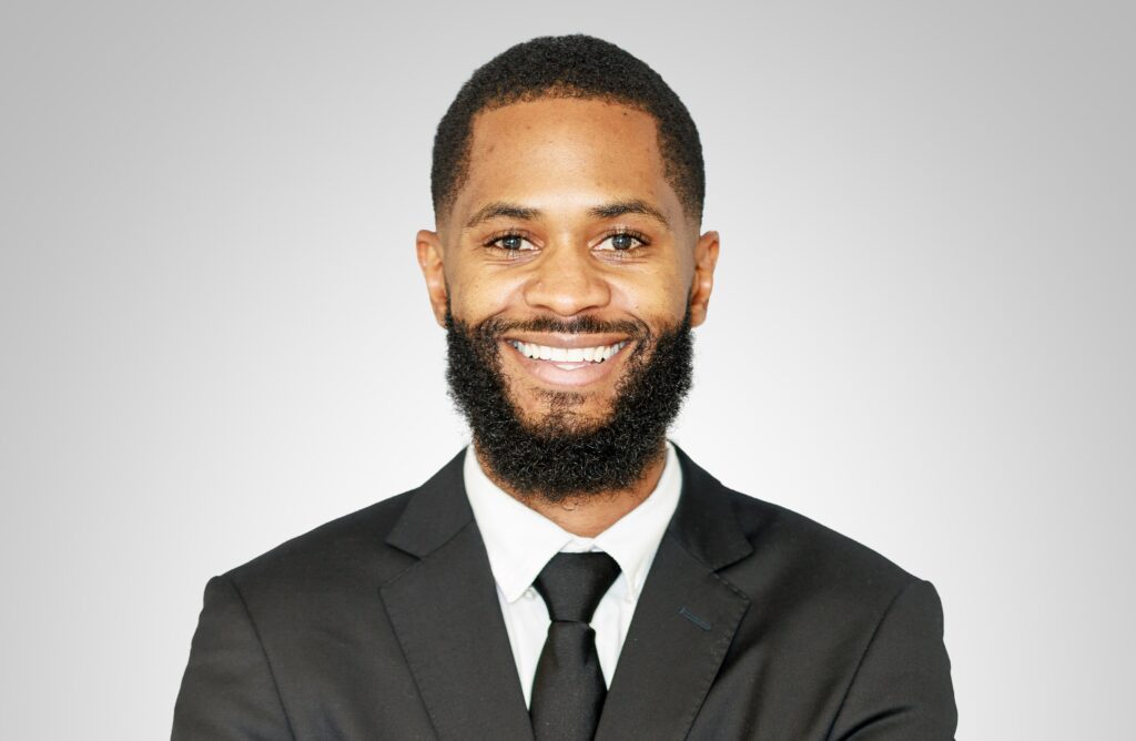 Vasco Victor - The Brief | Namibia's Leading Business & Financial News Smiling Black man in a suit and tie, portrait against a gray gradient background.