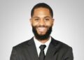 Smiling Black man in a suit and tie, portrait against a gray gradient background.