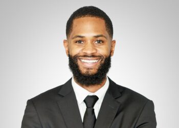 Smiling Black man in a suit and tie, portrait against a gray gradient background.