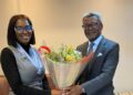 Two professionally dressed individuals exchange a bouquet of flowers in a bright, modern room.