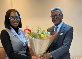 Two professionally dressed individuals exchange a bouquet of flowers in a bright, modern room.