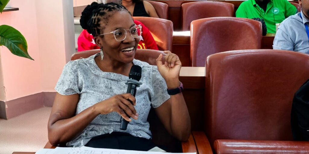 Paulina Shipahu - The Brief | Namibia's Leading Business & Financial News Smiling woman with glasses sits in a conference room, holding a microphone and speaking.