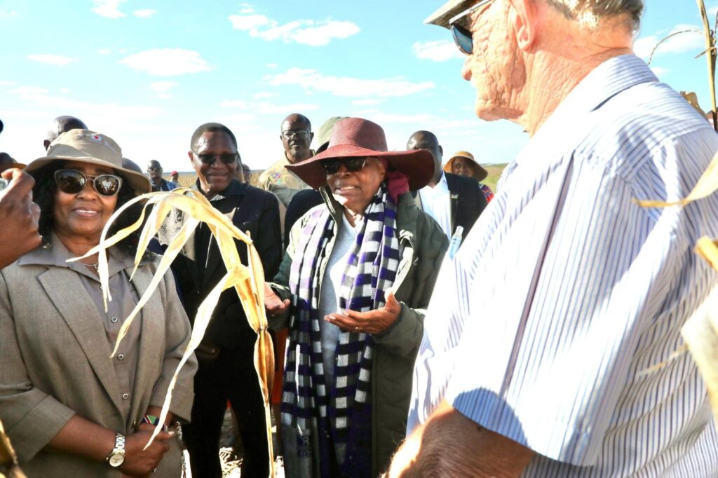Nandinaitwa - The Brief | Namibia's Leading Business & Financial News Group of people outdoors, a woman in a wide-brimmed hat and scarf speaks to a crowd while others listen in a sunny field.