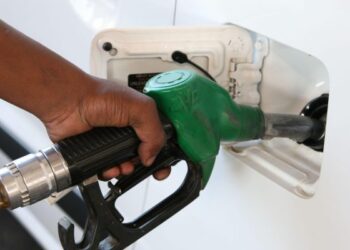 Close-up of a hand holding a green gas pump nozzle inserted into a white car's fuel door.