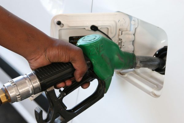 Close-up of a hand holding a green gas pump nozzle inserted into a white car's fuel door.