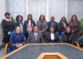 Govnment - The Brief | Namibia's Leading Business & Financial News Eleven professionals inBusiness formal clothing posing for a group photo in a conference room around a large table amid blue chairs and light curtains.
