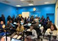 WhatsApp Image 2026-06-08 at 115257 AM - The Brief | Namibia's Leading Business & Financial News Adults in a computer lab seated at workstations while a group stands at the back of a blue-walled room.