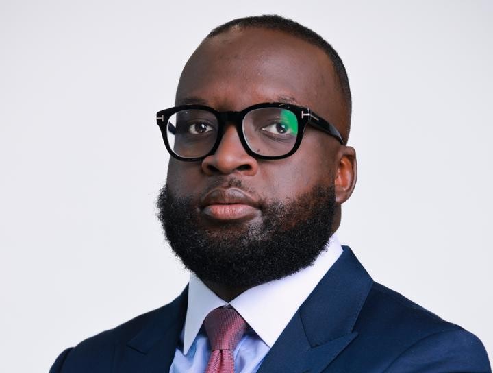 Leonard Hamunyela - The Brief | Namibia's Leading Business & Financial News Portrait of a bearded man in a navy suit, white shirt, burgundy tie, and black glasses against a light background, looking at the camera.