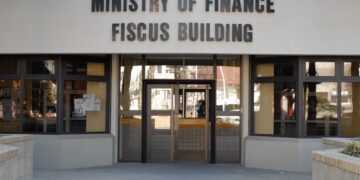 Front entrance of the Ministry of Finance, with a large sign reading 'MINISTRY OF FINANCE FISCUS BUILDING' above glass doors.