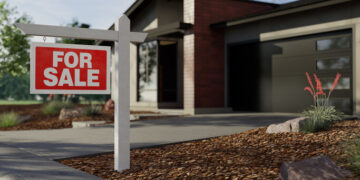 Red and white 'For Sale' sign on a white post in front of a modern house with a concrete driveway.