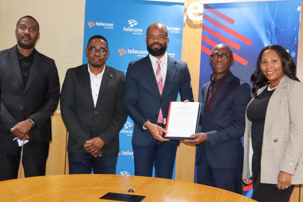 WhatsApp Image 2026-06-09 at 84216 AM - The Brief | Namibia's Leading Business & Financial News Five professionals pose at a telecom event; center man in navy suit holds a framed certificate.