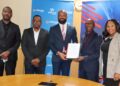 Five professionals pose at a telecom event; center man in navy suit holds a framed certificate.