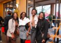 WhatsApp Image 2026-06-09 at 33214 PM - The Brief | Namibia's Leading Business & Financial News Four women smiling and posing for a photo at an indoor event, each holding a red gift bag or shopping bag, dressed stylishly.