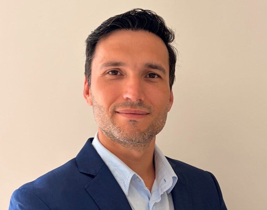 Henry Friedrich - The Brief | Namibia's Leading Business & Financial News Professional headshot of a man in a navy blazer and light blue shirt against a beige wall, smiling subtly.