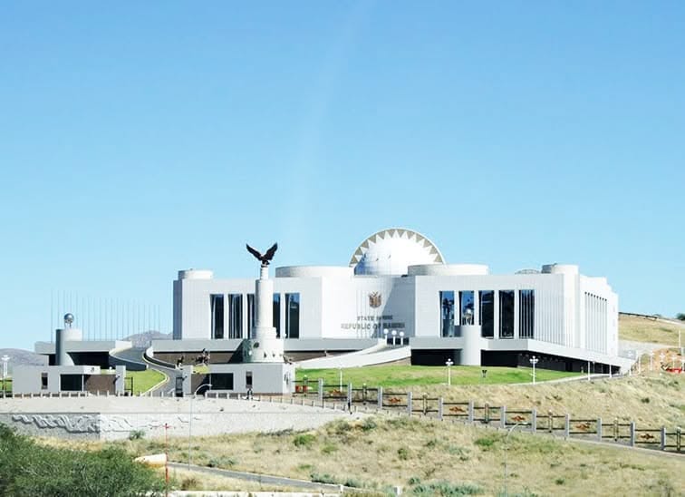 state house - The Brief | Namibia's Leading Business & Financial News White modern government building on a hill with a statue of an eagle on a pedestal in front, under a clear blue sky.