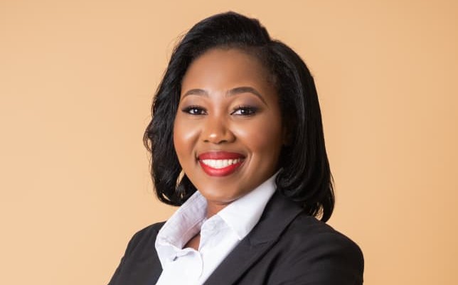 LISA MATOMOLA - The Brief | Namibia's Leading Business & Financial News Portrait of a smiling professional woman in a black blazer and white shirt against a beige background.