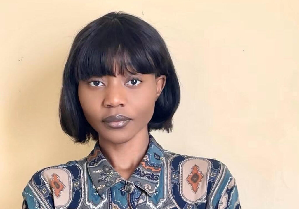 Tuwilika Nafuka - The Brief | Namibia's Leading Business & Financial News Portrait of a young woman with a short black bob and bangs, wearing a blue‑beige patterned shirt, standing against a pale yellow wall.