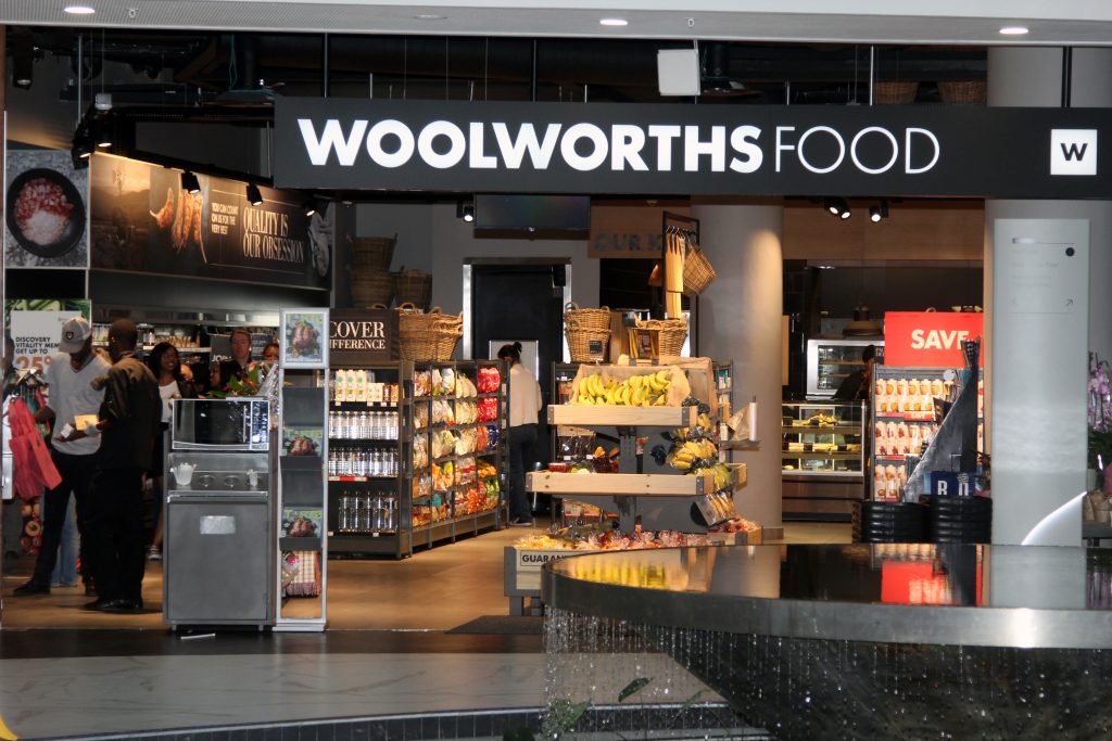 woolworths - The Brief | Namibia's Leading Business & Financial News Woolworths Food storefront interior with a central fruit and bread display and shoppers inside.