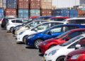 CARS1 - The Brief | Namibia's Leading Business & Financial News Row of colorful cars parked in a lot with stacked shipping containers in the background.