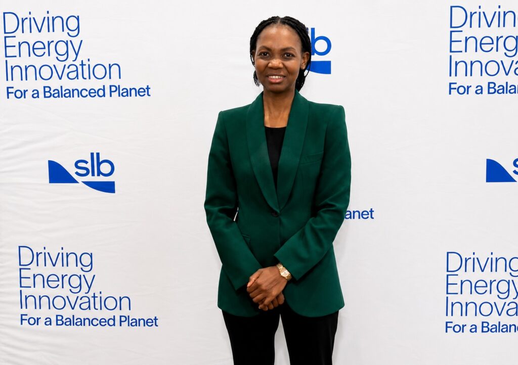 AUNE AMUTENYA - The Brief | Namibia's Leading Business & Financial News Woman in a green blazer stands in front of a white backdrop with 'Driving Energy Innovation' text and logos, hands folded.