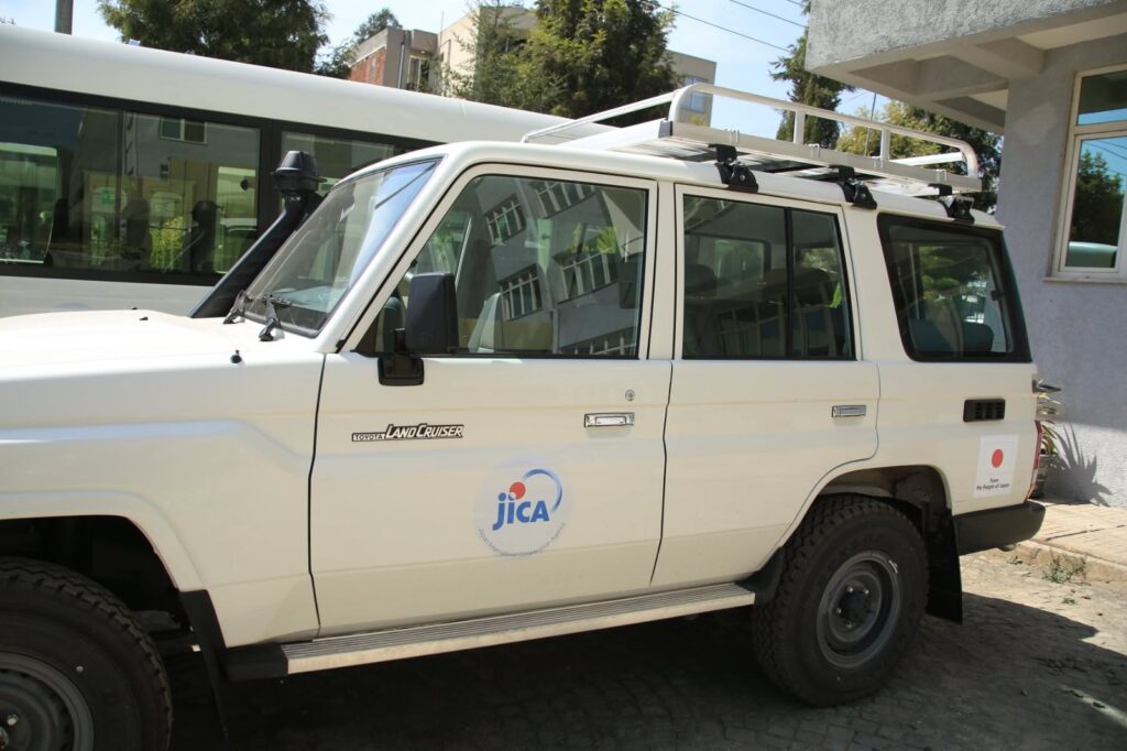 JICA - The Brief | Namibia's Leading Business & Financial News White Toyota Land Cruiser SUV with a roof rack, parked beside a building; door displays a JICA logo sticker and a small Toyota badge visible on the front panel.