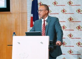 Man in teal suit delivers a presentation at a white podium with a Namibia Bank of Namibia backdrop