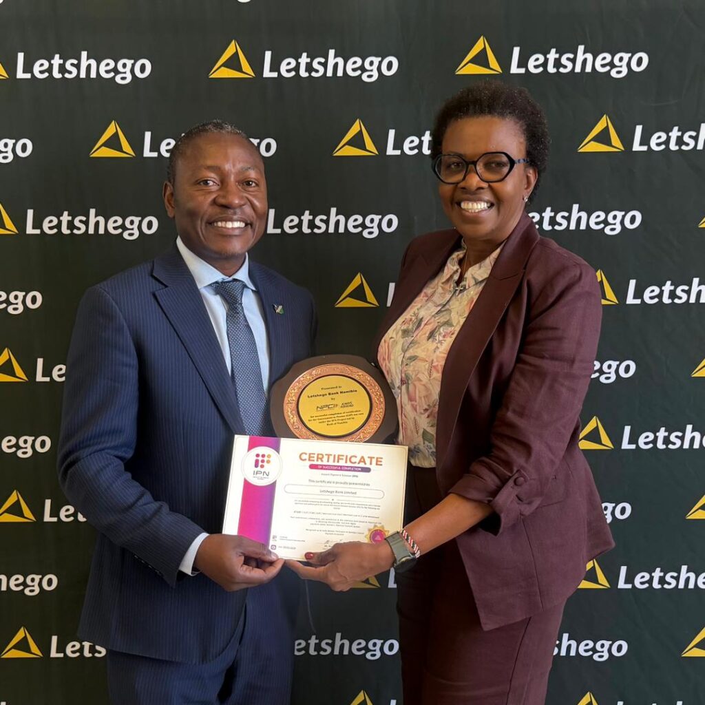 WhatsApp Image 2026-06-18 at 112735 PM - The Brief | Namibia's Leading Business & Financial News Two professionals in business attire smile as they hold a circular trophy and a certificate together in front of a Letshego-branded backdrop.