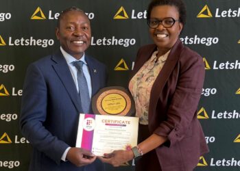 Two professionals in business attire smile as they hold a circular trophy and a certificate together in front of a Letshego-branded backdrop.