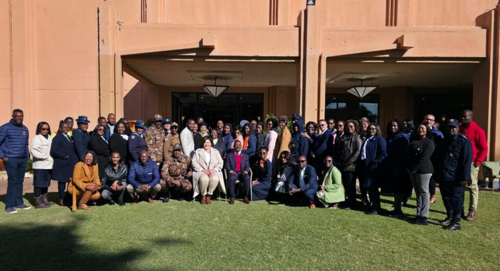 WhatsApp Image 2026-06-23 at 102305 AM - The Brief | Namibia's Leading Business & Financial News Large diverse group of adults posing for a group photo on a green lawn in front of a peach-colored building entrance.