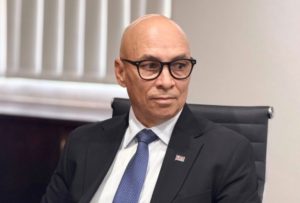 BRIAN EISEB3 - The Brief | Namibia's Leading Business & Financial News Professional man in a dark suit and blue tie seated in an office chair, looking to the side, wearing glasses and a lapel pin