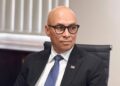 BRIAN EISEB3 - The Brief | Namibia's Leading Business & Financial News Professional man in a dark suit and blue tie seated in an office chair, looking to the side, wearing glasses and a lapel pin