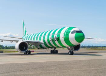 Condor commercial jet with bold green-and-white stripes sits on the taxiway under a clear blue sky, engines visible and ready for departure