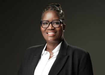 Professional woman in a black blazer and white shirt, wearing glasses, smiling for a corporate headshot.