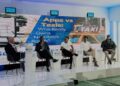 Panel discussion on a stage with five men seated; large screen behind reads 'Apps vs Taxis: Who Really Owns Namibia's Roads?'