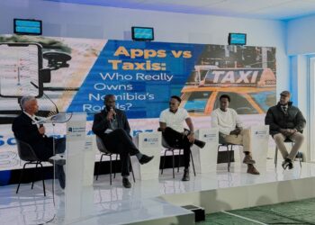 Panel discussion on a stage with five men seated; large screen behind reads 'Apps vs Taxis: Who Really Owns Namibia's Roads?'