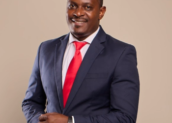 Smiling man in a navy suit and red tie posing with hands clasped
