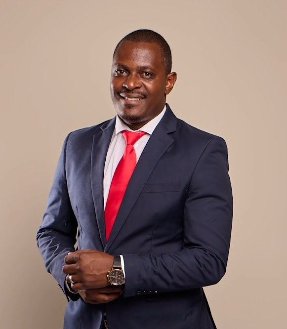 Josephat Kustaa_The Brief_Image - The Brief | Namibia's Leading Business & Financial News Smiling man in a navy suit and red tie posing with hands clasped