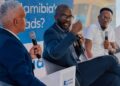 gov public transport - The Brief | Namibia's Leading Business & Financial News Panel of three men in suits on stage, each holding a microphone; blue banner behind reads 'Who Really Owns ...' with taxi imagery in the background.