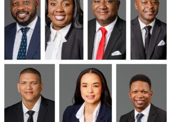 Group of eight diverse professionals shown in formal headshots against a gray background, in business attire.