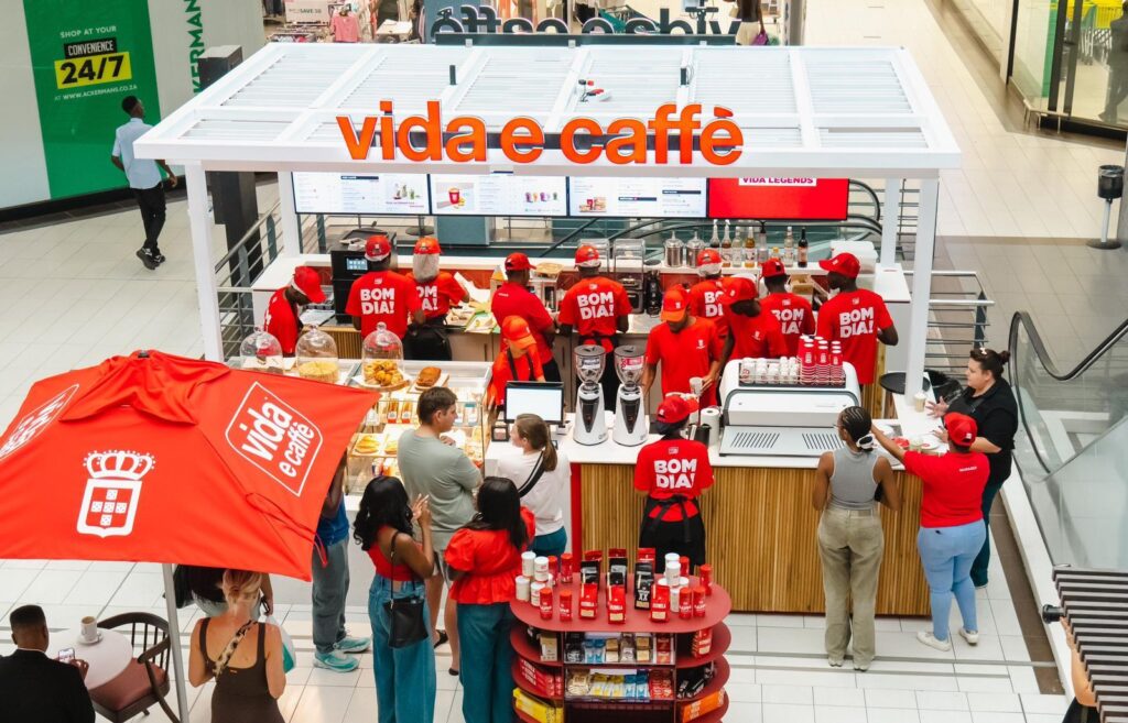 Busy Vida e Caffè kiosk in a mall, staff in red uniforms serve customers at the counter with coffee machines and pastries on display.