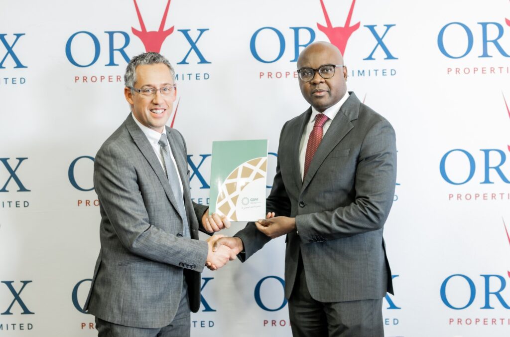 WhatsApp Image 2026-06-29 at 80000 PM - The Brief | Namibia's Leading Business & Financial News Two businessmen in gray suits shake hands as one passes a green folder at a corporate event with ORX logos behind them behind the backdrop.