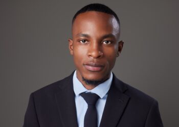 Evoto - The Brief | Namibia's Leading Business & Financial News Portrait of a young man in a dark suit and blue tie against a gray background.