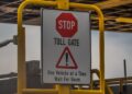 TOLL GATE - The Brief | Namibia's Leading Business & Financial News Stop toll gate sign: red octagonal 'STOP', 'TOLL GATE' with a warning triangle and text: 'One Vehicle at a Time, Wait For Boom'