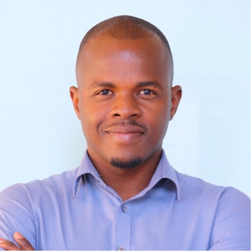Mr Michael Neema - The Brief | Namibia's Leading Business & Financial News Portrait of a man with short hair and a goatee, smiling in a light blue button-down shirt against a pale blue background.