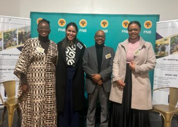 Four professionals posing and smiling at a corporate event with FNB banners in turquoise behind them, name tags visible.