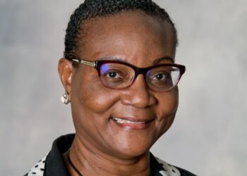 Smiling Black woman wearing glasses and a black blazer with a white polka-dotted collar.