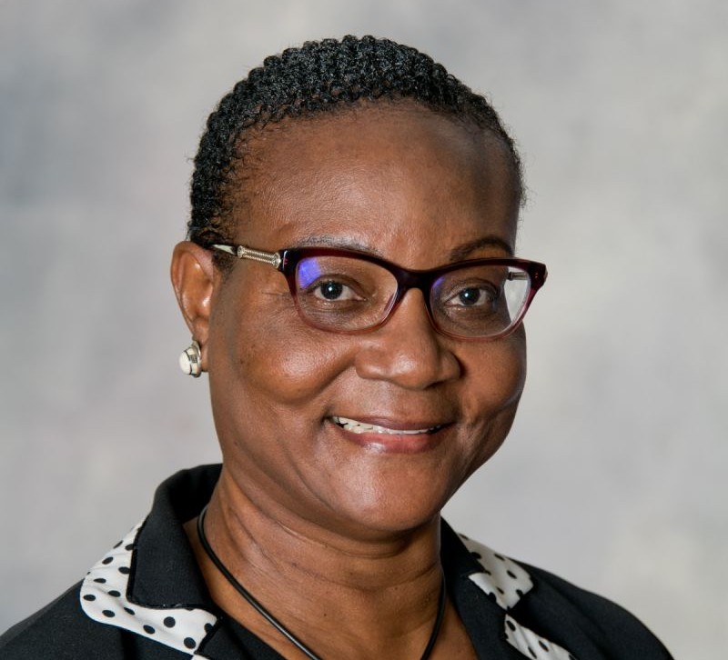Smiling Black woman wearing glasses and a black blazer with a white polka-dotted collar.