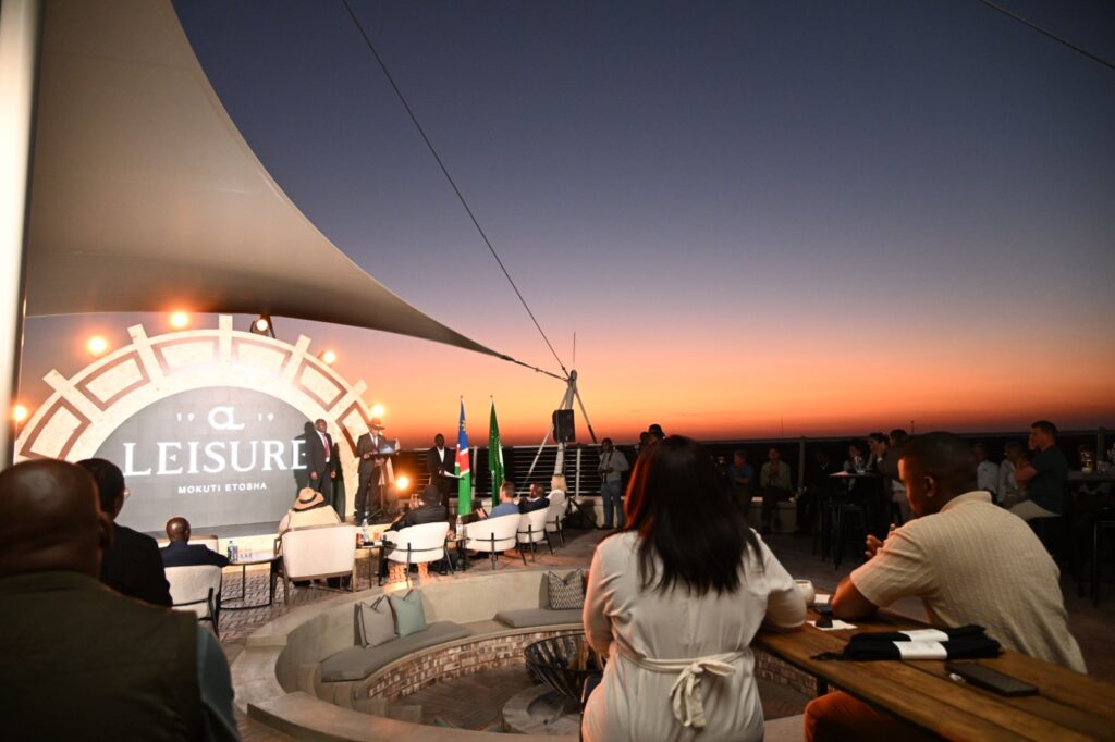 Rooftop evening event with a stage, large circular ‘Leisure’ backdrop, and audience seated around tables at sunset.
