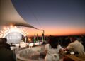 OL LEISURE - The Brief | Namibia's Leading Business & Financial News Rooftop evening event with a stage, large circular ‘Leisure’ backdrop, and audience seated around tables at sunset.